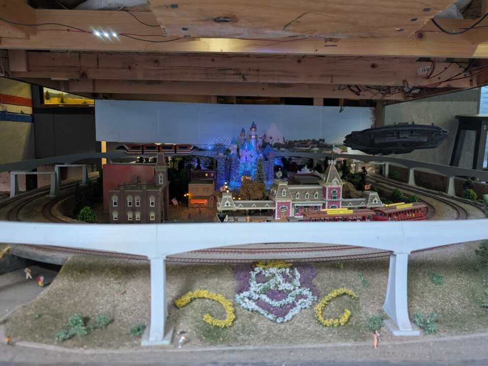 A miniature model of an amusement park, with an elevated tram track and a mascot of a cartoon mouse in front.