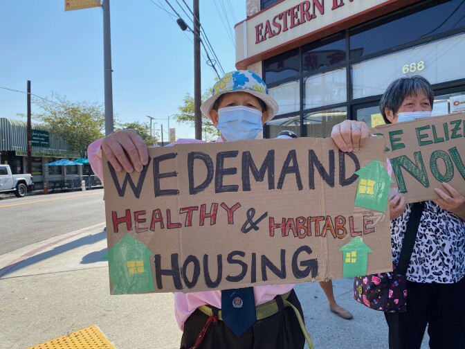  man wearing a hat and face mask holds a protest sign that reads "We demand healthy and habitable housing."
