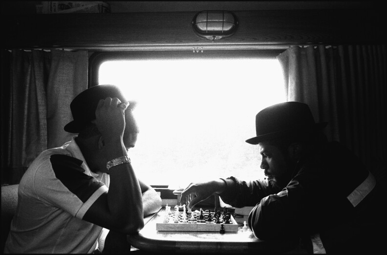 Two men in hats play checkers next to a window.