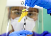 A person protective gear holds a syringe and draws liquid out of a vile.