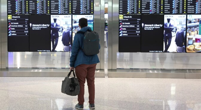a person with a backpack and a bag looks at a board of flight information