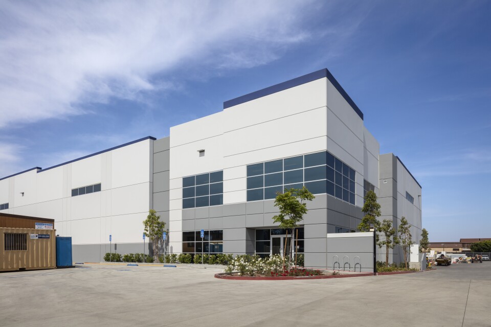 A large white and gray warehouse under a blue sunny sky. 