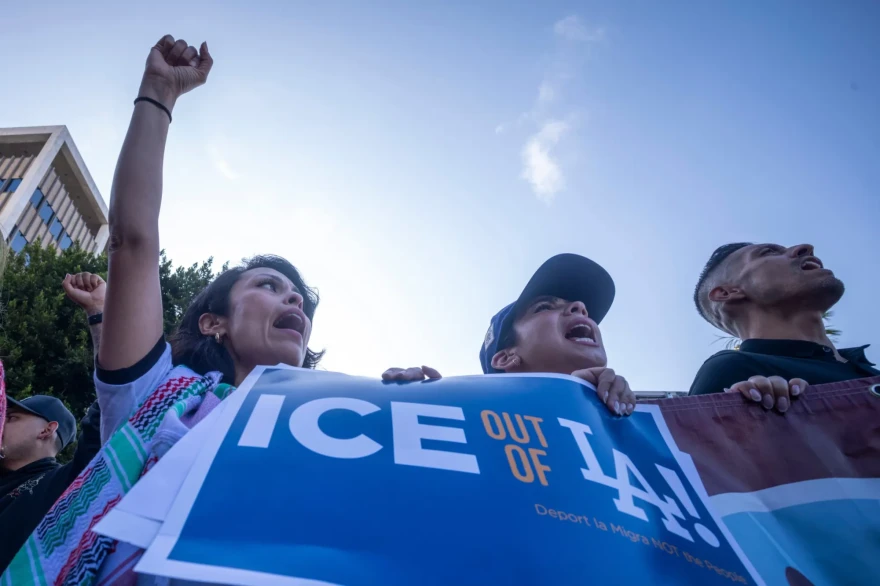 A group of protesters raise their fists and hold a banner that reads "ICE out of LA!" during a demonstration.