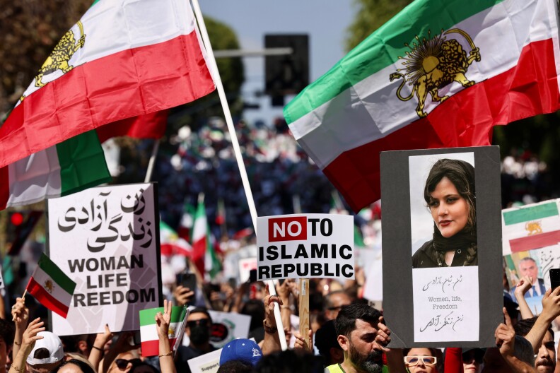Protesters hold flags, signs and an image of Masha Amini with the words in English and Farsi: Women, life, Freedom