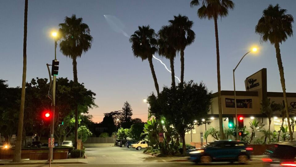 A burst of light is seen in a trail over palm trees and buildings