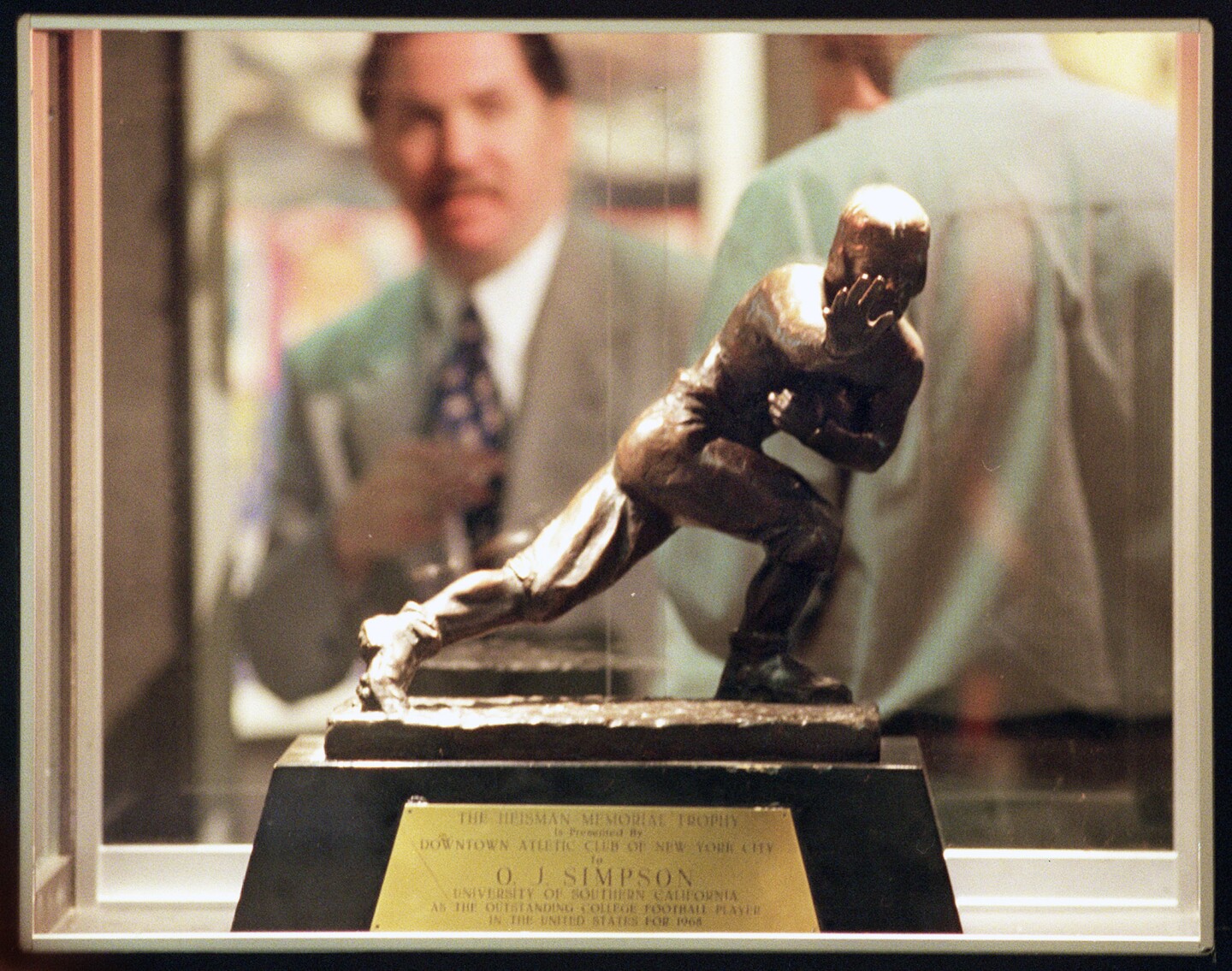 File: Michael Schwartz, director of entertainment memorabilia for the auction house of Butterfield & Butterfield, is seen through a display case containing O.J. Simpson's 1968 Heisman Trophy at their gallery in this Feb. 10, 1999 file photo, in Los Angeles. Los Angeles police say they've recovered a Heisman Trophy honoring O.J. Simpson more than 20 years after it was stolen from the University of Southern California.
