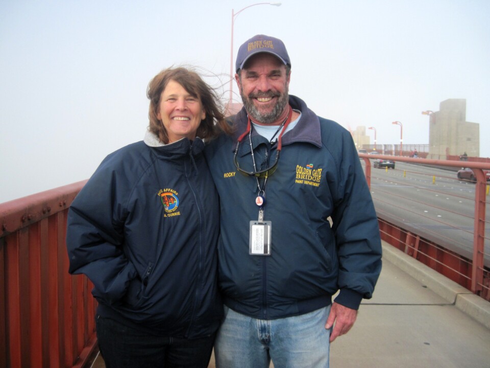 Golden Gate Bridge spokeswoman Mary Currie and paint superintendent Rocky Dellarocca stand on the bridge. The orange cables behind them are obscured by thick fog. From July to October, foghorns blare for more than 5 hours a day on average.