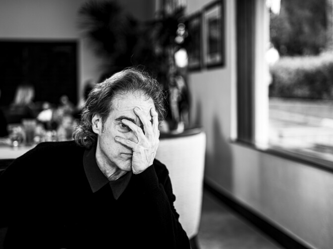 A photo of a man sitting at a dinner table, covering his face with one hand
