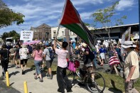A crowd of protesters march on the sidewalk and the street in Pasadena. Many of them carry signs and flags.