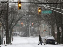 A woman pulls a cart as she walks across the street covered with snow, Tuesday, Jan. 21, 2014, in Jersey City, N.J. A storm is expected to hit the northern New Jersey region throughout the day. Because of hazardous driving conditions New Jersey Gov. Chris Christie's inauguration party at Ellis Island was cancelled. (AP Photo/Julio Cortez)