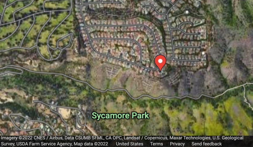 An overhead satellite view of a map with green space labeled Sycamore Park to the south and a residential neighborhood, tan-colored, to the north.