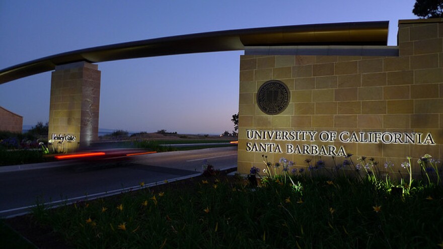 A large cement wall beside a highway at night. On the wall is illuminated lettering that reads: "University of California Santa Barbara."