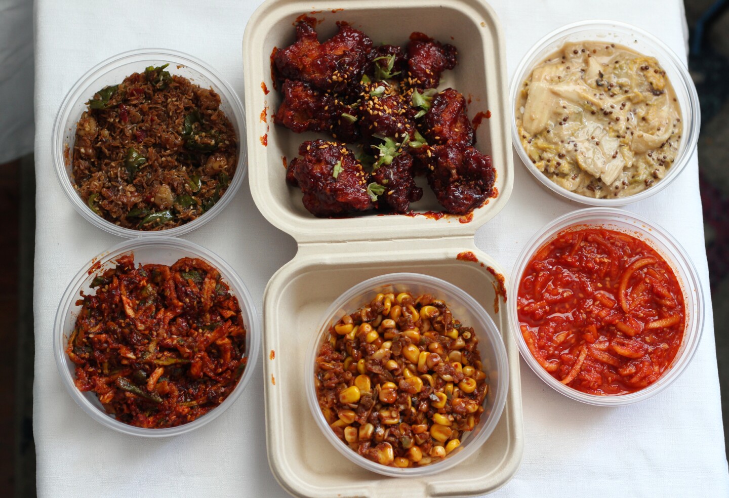 bowls of red spicy pastes and dips, a bowl of corn kernels and bright red fried chicken