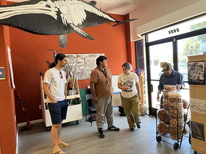 Members of Coyotl+Macehualli stand in the lending library as a local street vendor enters to sell them some sweet bread.