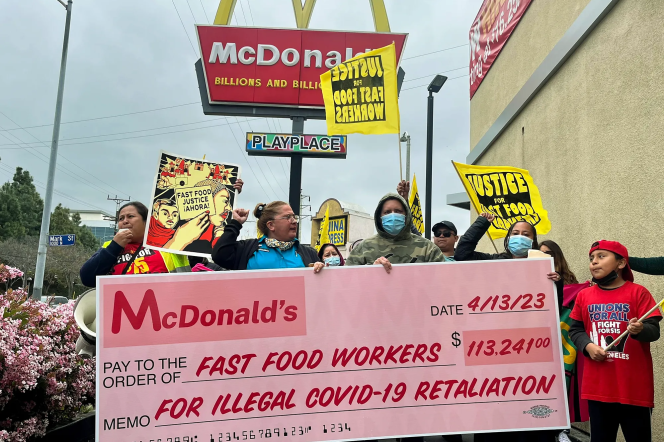 A group of protesters hold up a large replica check that says McDonald's 4/13/23 Pay to the Order of Fast Food Workers $113,241 Memo For Illegal COVID retaliation