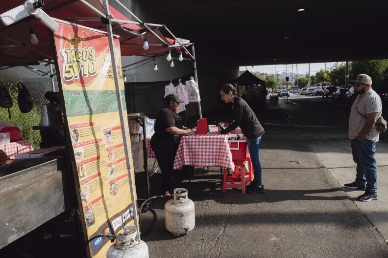 Two customers line up at a food stand underneath the freeway.