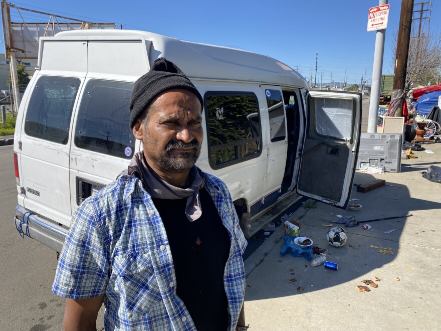 Quentin Rodriguez, who is an unhoused man, is standing outside his white camper van parked on a street in Sun Valley, CA.