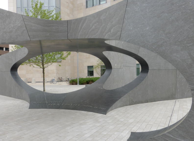 A large abstract environmental sculpture located in the middle of a paved area on MIT.