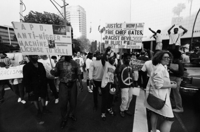 File: A group of people hold up signs advocating changes in the Los Angeles Police Department during the LA Riots unrest on April 29, 1992.