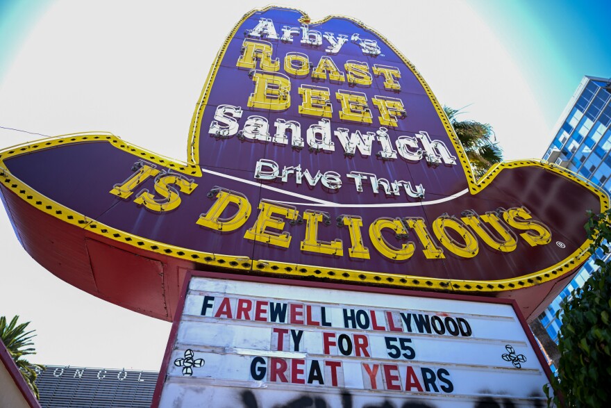 A close-up of a huge red and yellow neon Arby's sign pictured from below. The sign has red and black letters that read "Farewell Hollywood TY For 55 Great Years"