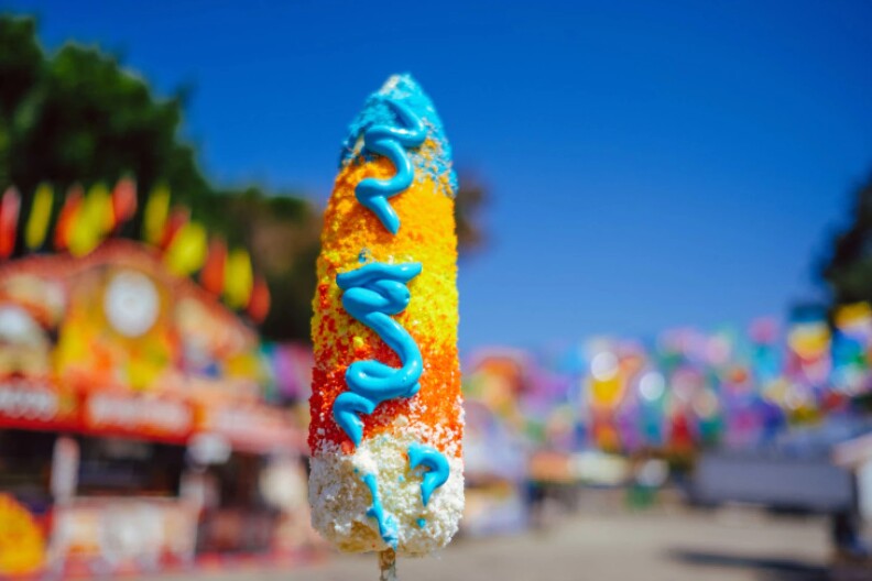 An ear of corn has been covered with rainbow-colored stripes and blue mayonnaise. 