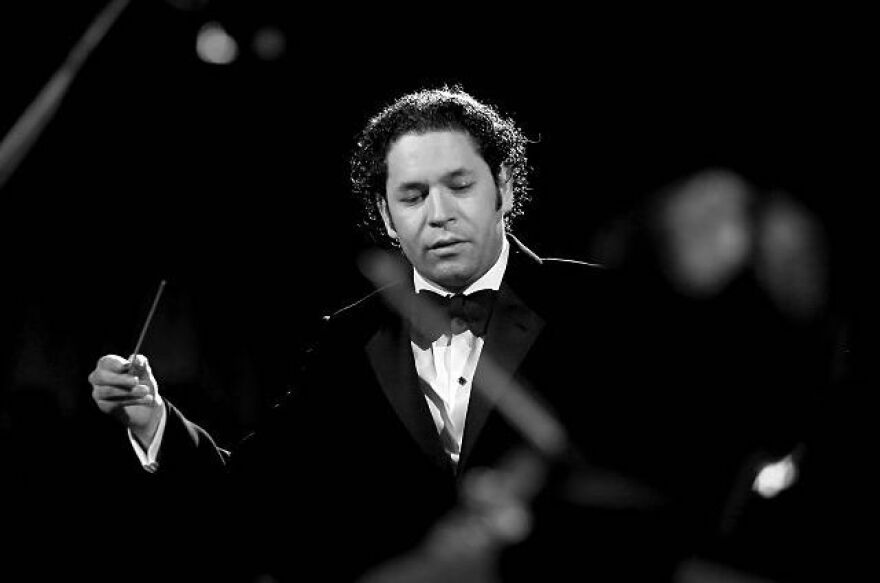 A man with curly hair is in a black tux and using a conductors baton.