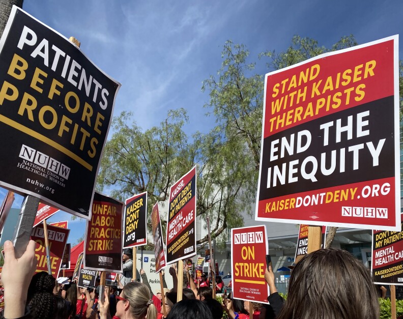Picketers hold high red, yellow and black strike signs. They read: "Stand with Kaiser therapists" and "Patients before profits" 
