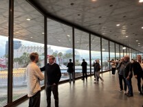 Museum attendees mill around the cement and glass interior of the David Geffen Galleries. In the background, illuminated street lights from the Urban Light public art installation are visible, along with palm trees and other museum buildings.