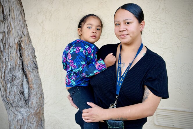  A medium skin-toned woman in a black top and a young medium skin-toned girl in a brightly patterned jacket stand together, the woman holding the girl close.