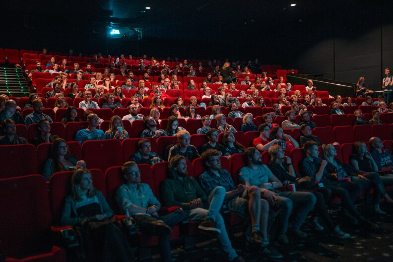 An audience of people sitting in red movie theater seats, all watching the screen.