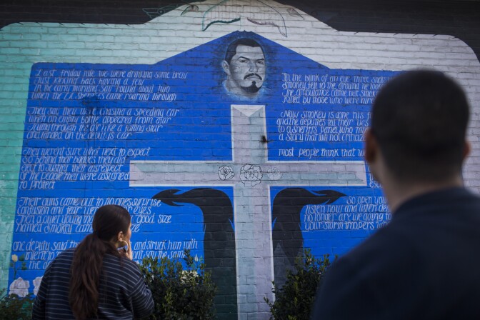 Amanda Gutierrez, left, and Eddie Licon look at a mural in Ramona Gardens in Boyle Heights memorializing a community member killed by police in the 1990s.