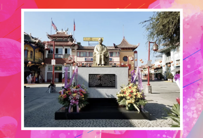 A statue of a seated man on a large cube pedestal, with flower arrangements in both sides, in an open square or plaza. Behind it are traditional Chinese-style buildings.