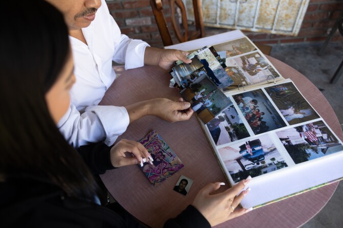 A man and a woman sit at a table, looking at an open photo album.