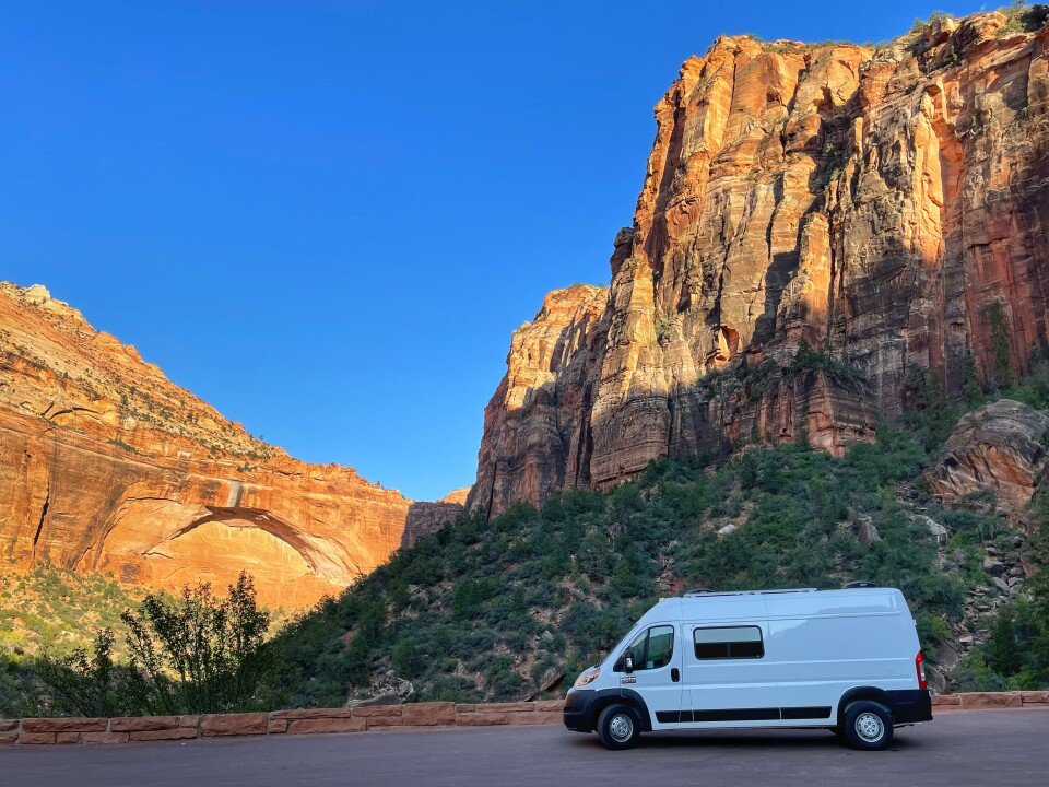 A van driving down a rode with red rock mountains in the background