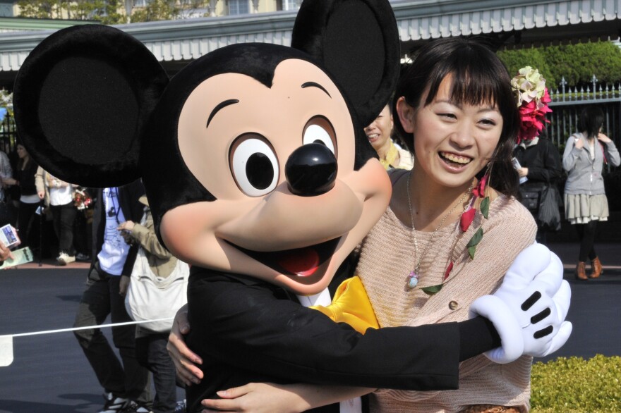 A life size Mickey Mouse is hugging a smiling woman