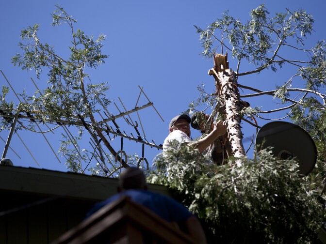 Works try to dislodge tree branches from antennae on the roof of a home in Forest Falls after a flash flood and mudslide covered the community in debris.