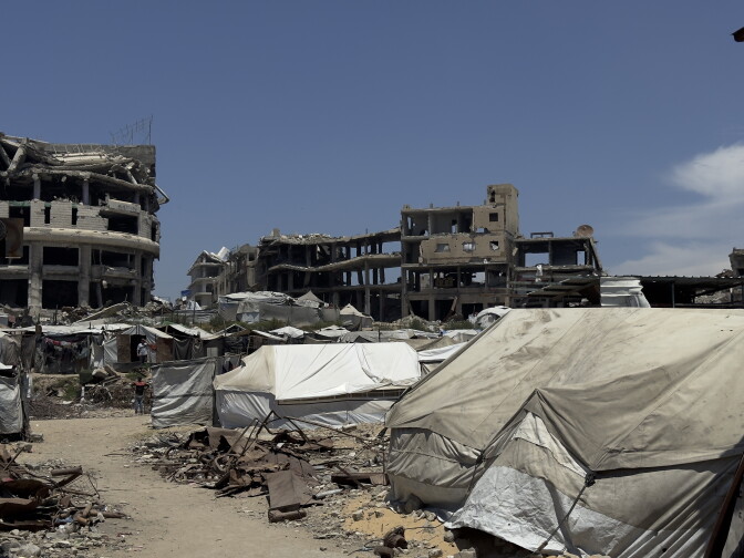 White and grey tents stand amid the rubble of destroyed homes and buildings.