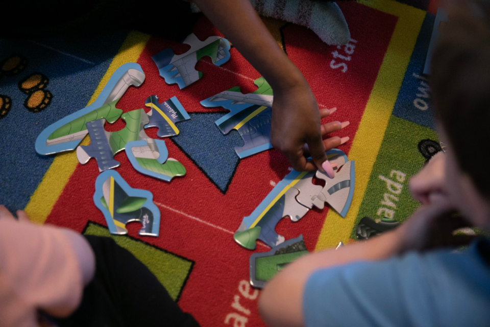 Aerial view of a colorful carpet with hands working on a puzzle with big pieces.