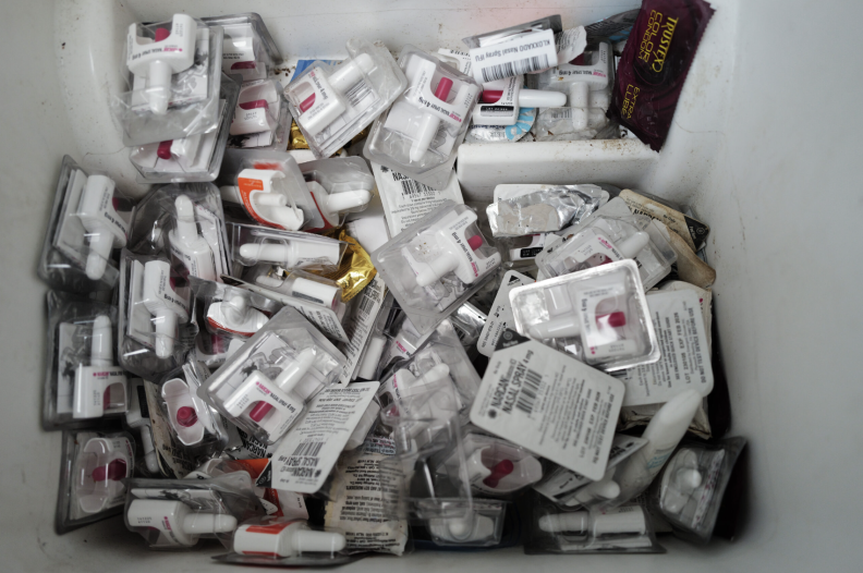 A top-down shot of a bin full of plastic-packaged naloxone (Narcan) spray medication.