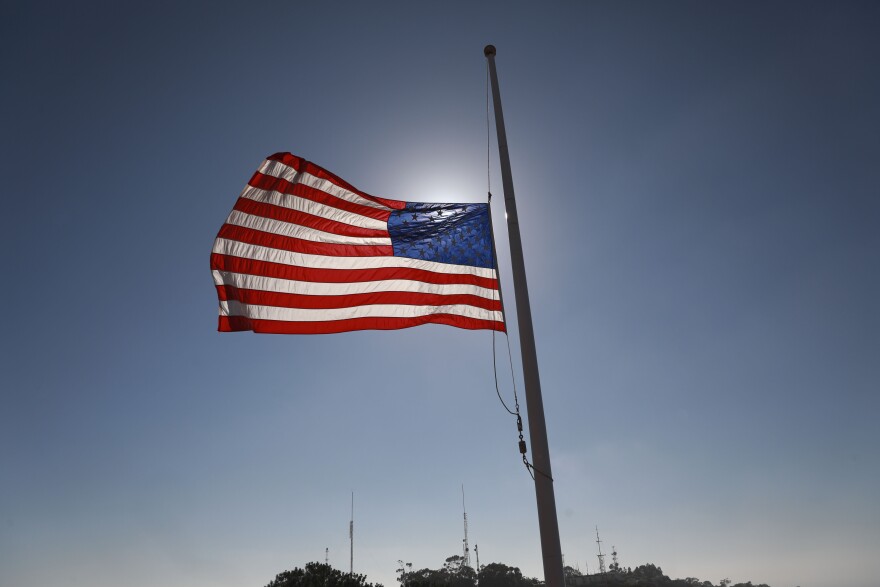 An American flag flies at half-staff in the wind with a blue sky in the backround.