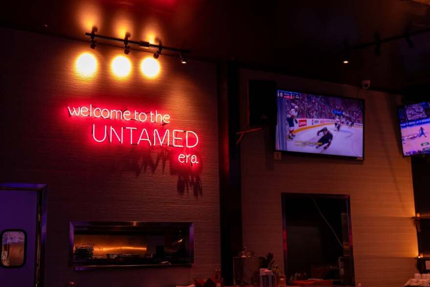 A pink light up sign reads "Welcome to the Untamed era" is seen on a wall next to a television in the Untamed Spirits bar in Silver Lake.