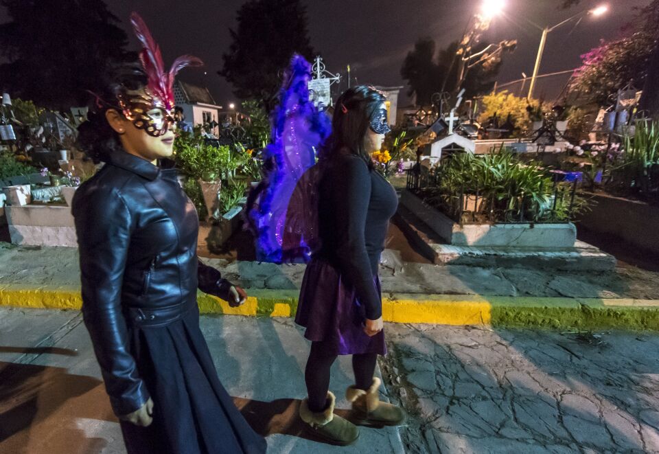 Two young women in costumes pass through graves at the San Francisco Cemetery in Mexico City on November 1, 2016.