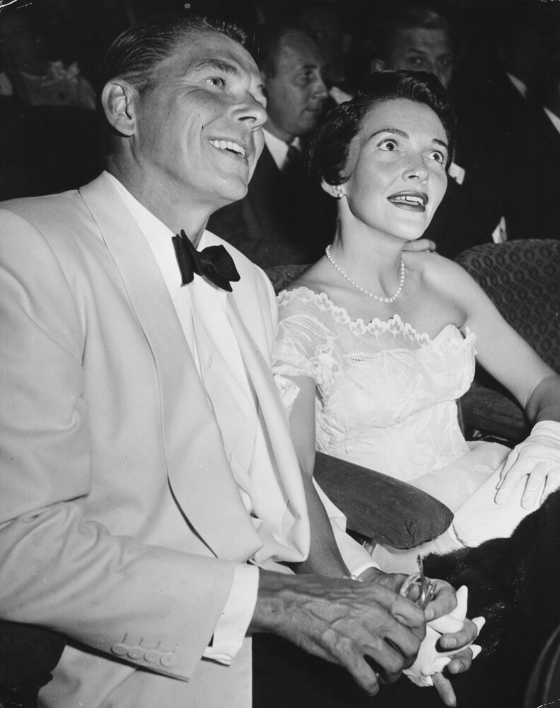 Actor Ronald Reagan and his wife Nancy sitting together holding hands at a party in Hollywood circa 1955.