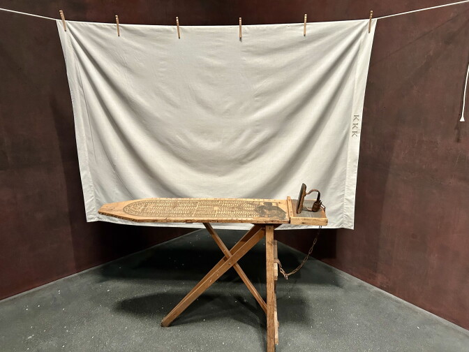 A white sheet hangs behind a vintage ironing board.