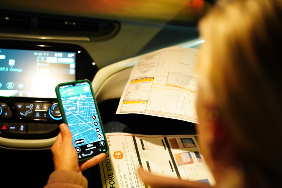 A woman uses a map app on her phone from the passenger seat of a car.