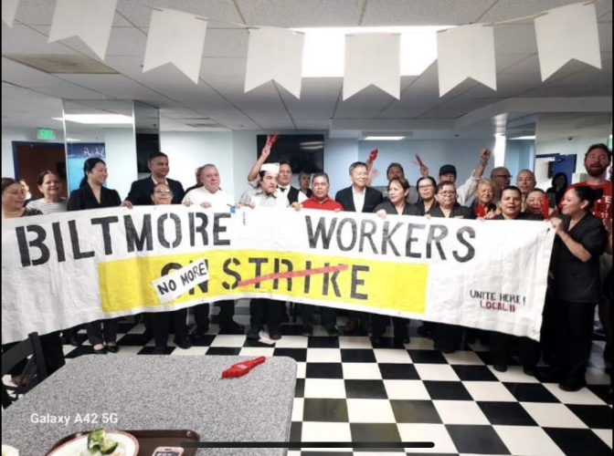 A crows of hotel workers gather behind a large banner with the words "Biltmore workers no more strike" as several in th ebackground raise their hands in celebration.