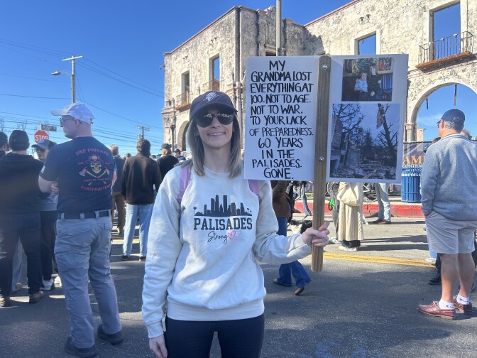 A woman holds a protest sign that reads in part "My grandma lost everything ... 60 years in the Palisades gone."