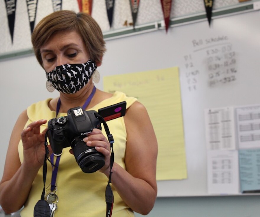 High School journalism teacher Adriana Chavira holds a camera inside a classroom.