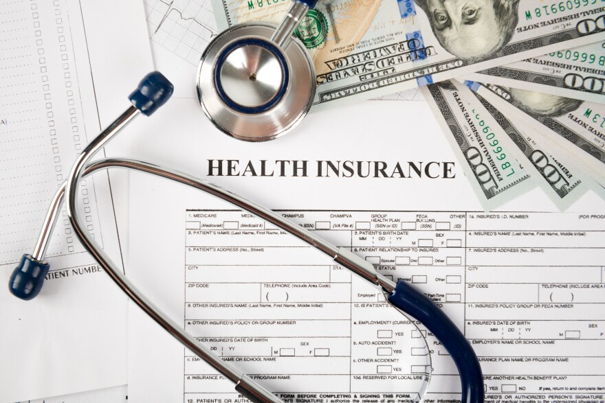 An array of items includes a stethoscope, health insurance form and $100 bills.