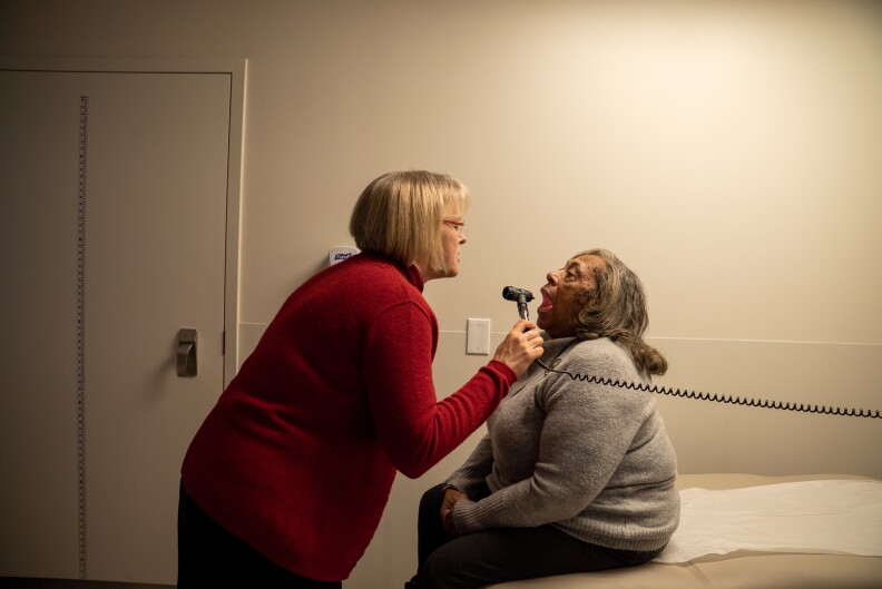 A doctor uses a tool to look inside the mouth of a patient.